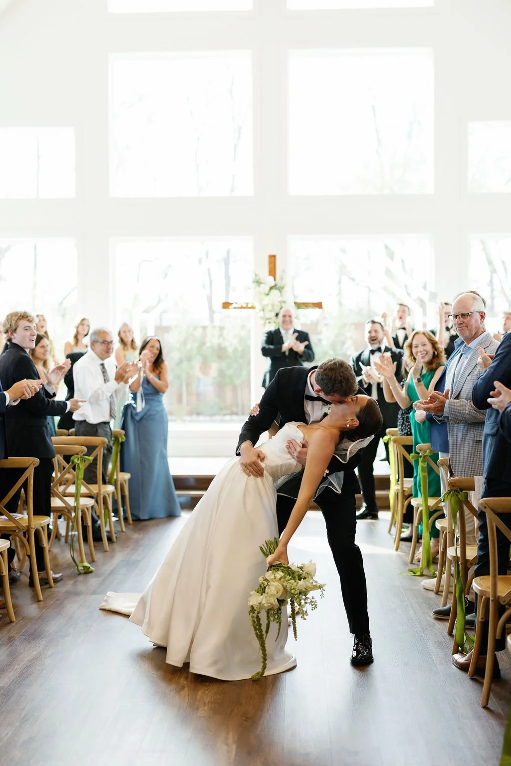 A wedding ceremony at River Road Venue, with the groom dipping his bride, as she holds an all white bridal bouquet