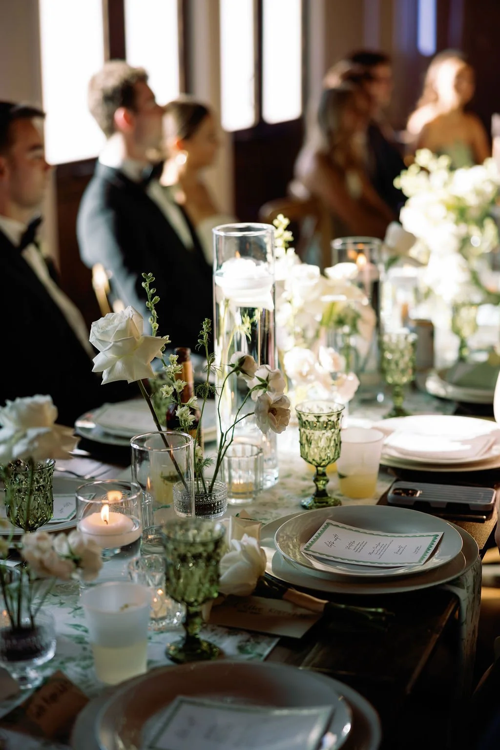 Details of white plates with a square menu on top, with scallop details, greenery patterned table runners, and bud vases by Haute Poppies Floral