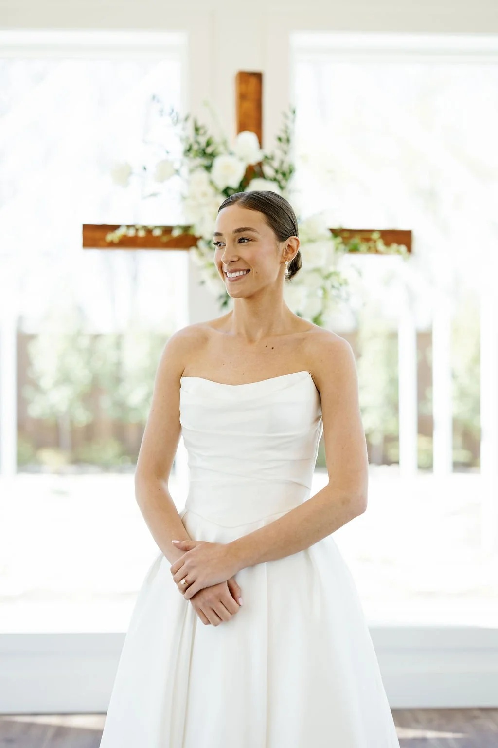Bridal portraits at River Road Venue in the chapel, with floor to ceiling windows, and a wooden cross covered in white flowers