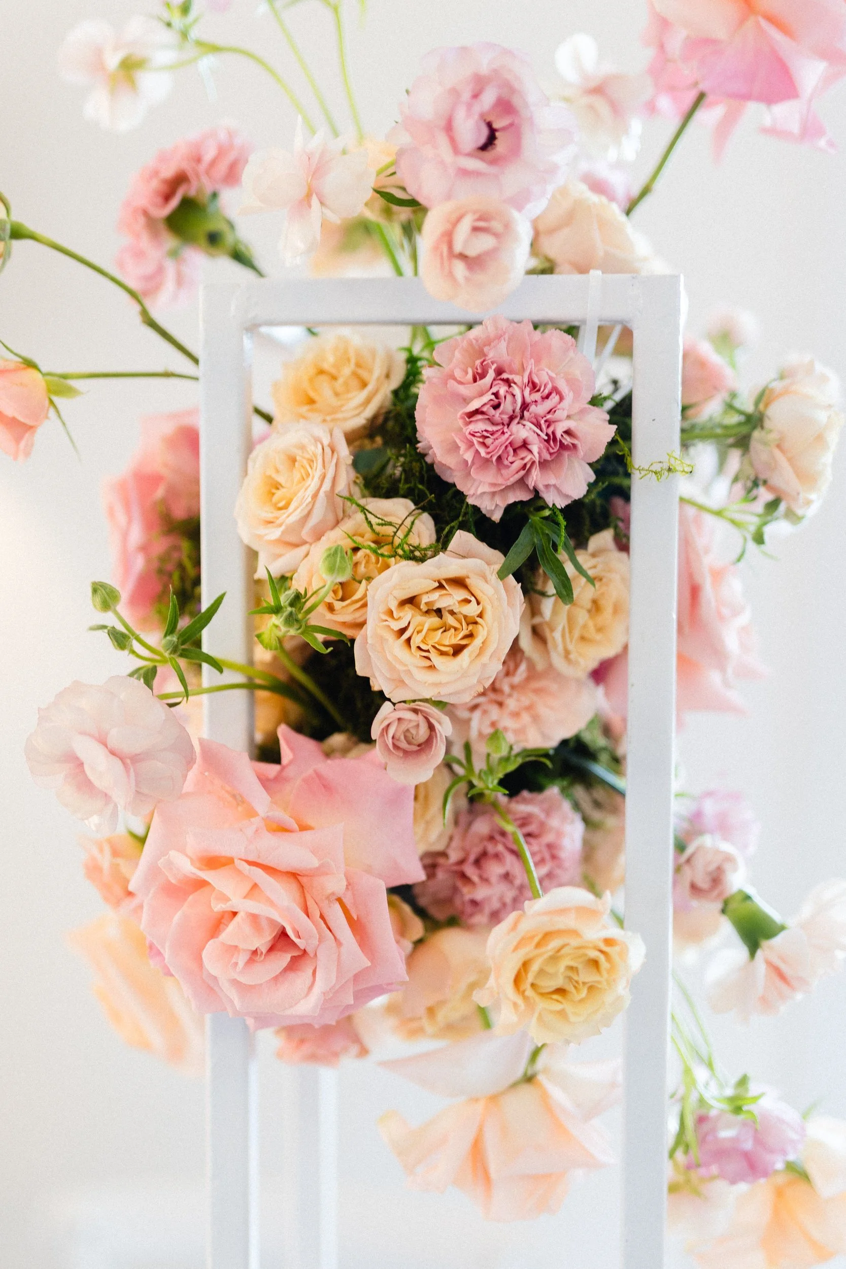 Close view of a white frame wrapped in blush and peach roses and airy pink blooms