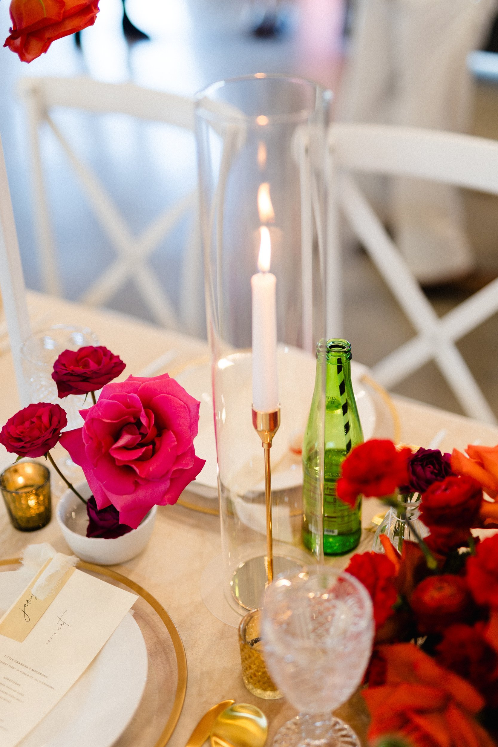Reception table with candles, glassware and low red and pink rose arrangements