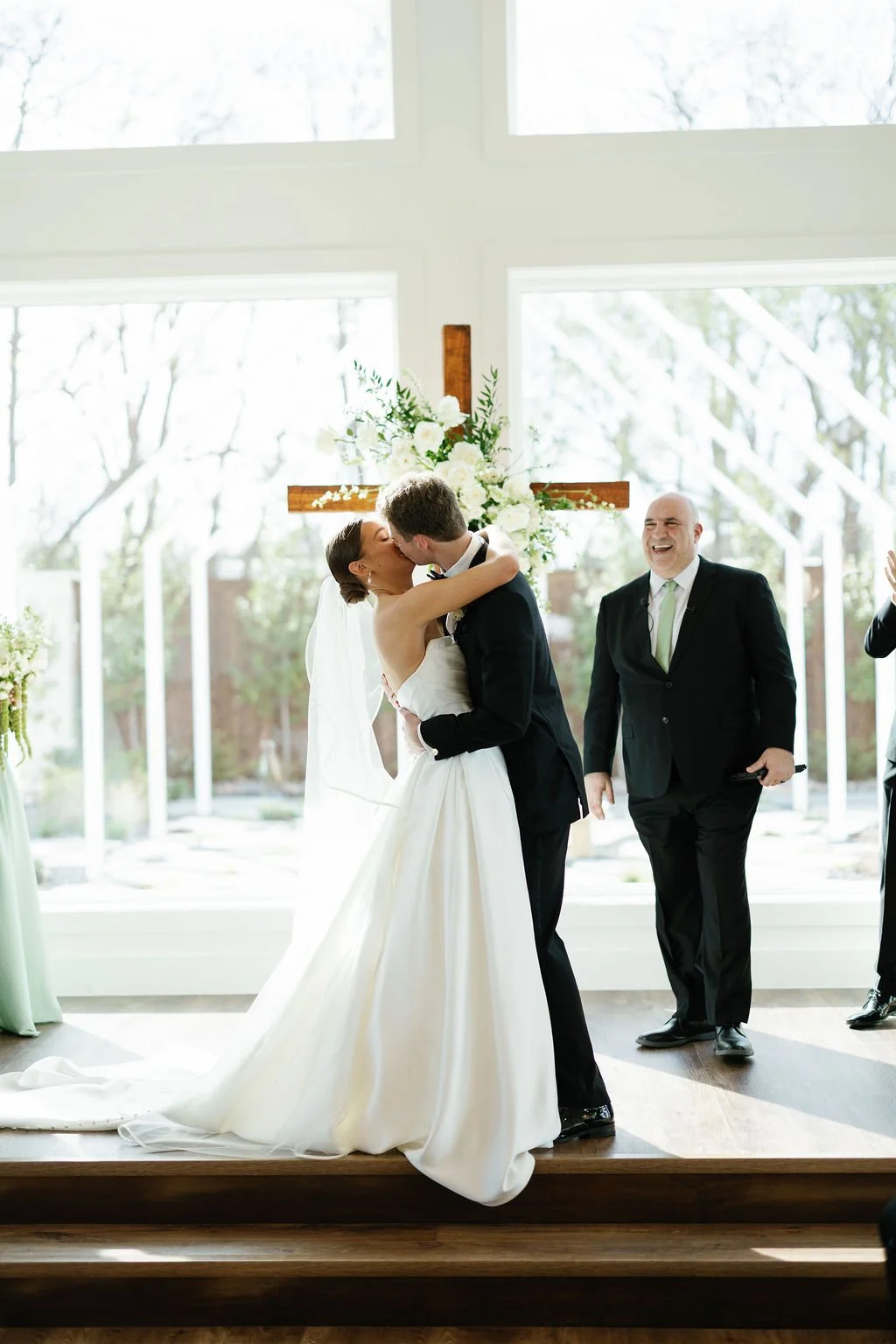 A first kiss after a wedding ceremony at River Road Venue, with the large windows behind them
