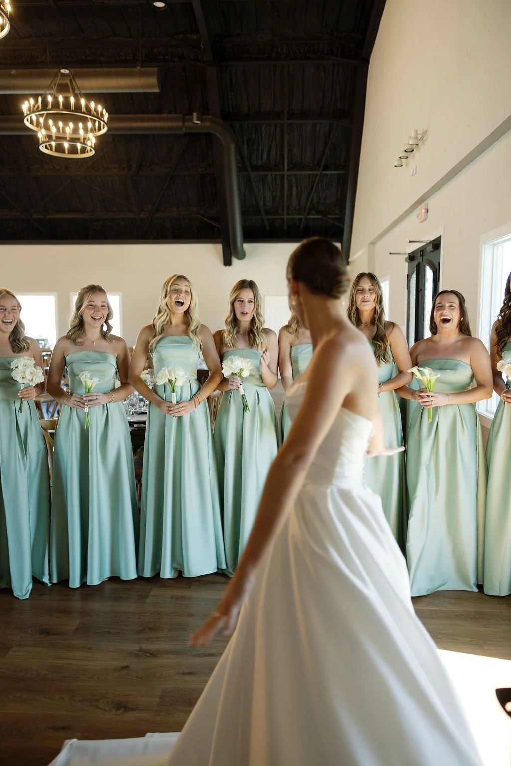 A bride and bridesmaids first look at River Road Venue, with the bride in a satin ballgown, the bridesmaids in satin sage dresses