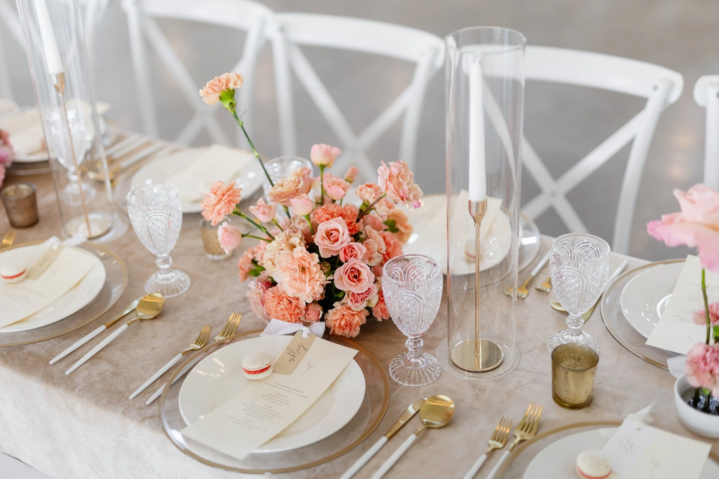 Reception place setting with gold flatware and a low peach and blush rose centerpiece