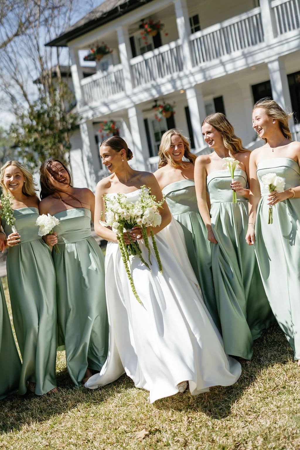 Bride and bridesmaids taking pictures at a venue in Texas, with the bride holding an all white bouquet with white garden roses, lisianthus, and trailing green hanging amaranthus