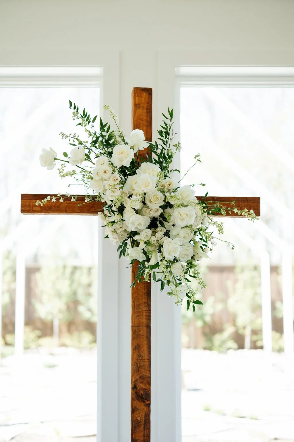 A wooden cross covered in white roses and flowers, by Haute Poppie Floral