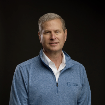 Man in blue sweater with company logo on dark background