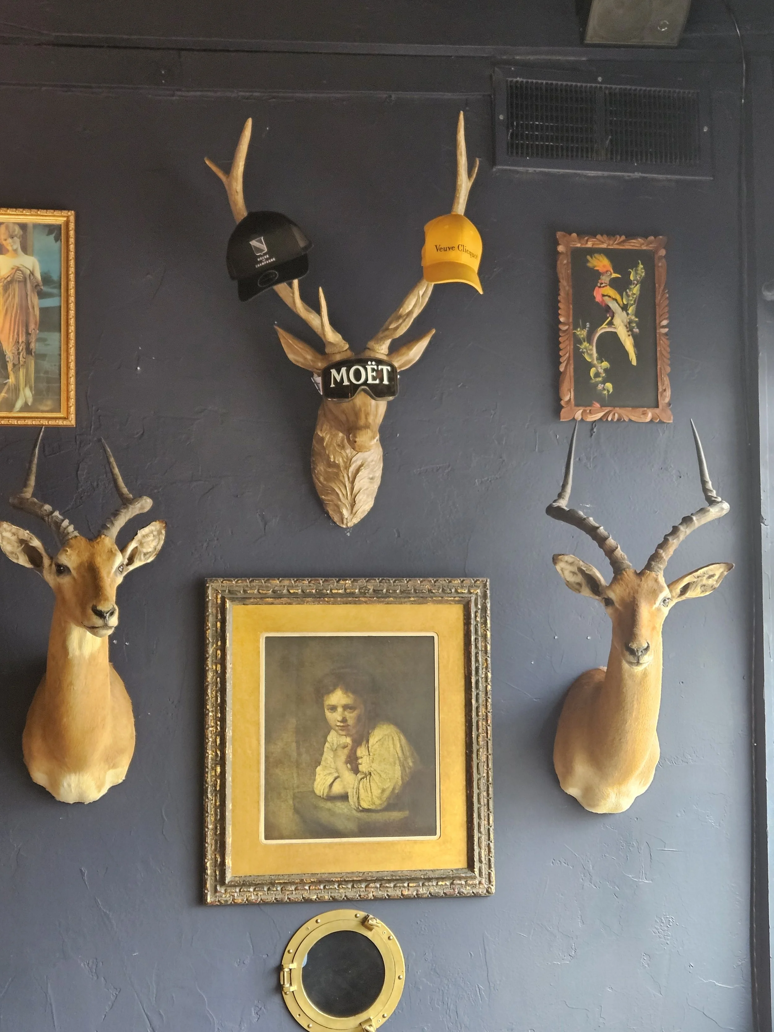 Interior wall decorated with two mounted Impala heads, a framed picture of a woman below and a smaller round porthole window at the bottom.