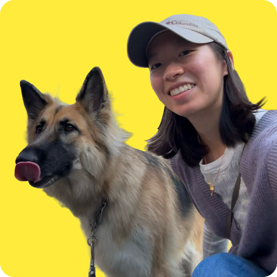 A smiling young woman wearing a light-colored baseball cap and a necklace, sitting next to a large German Shepherd dog with a tan and black coat, against a bright yellow background.