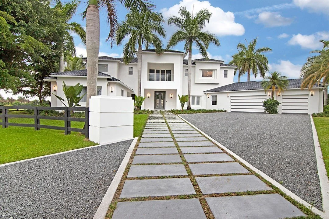 Modern two-story white house with palm trees, a concrete and gravel driveway, and a concrete pathway leading to the front door.