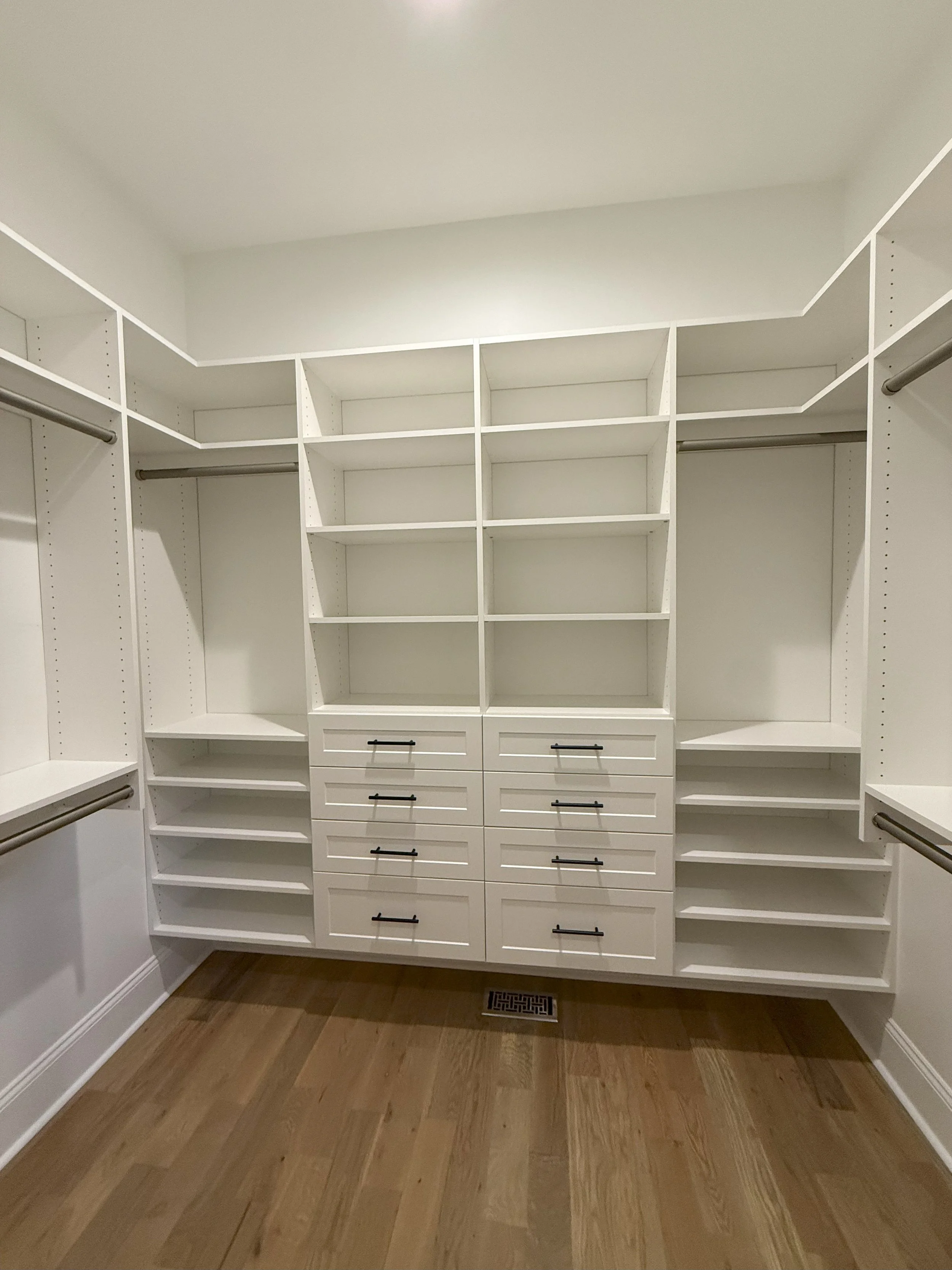 Empty white walk-in closet with shelves and drawers, hardwood floor, and a floor vent.