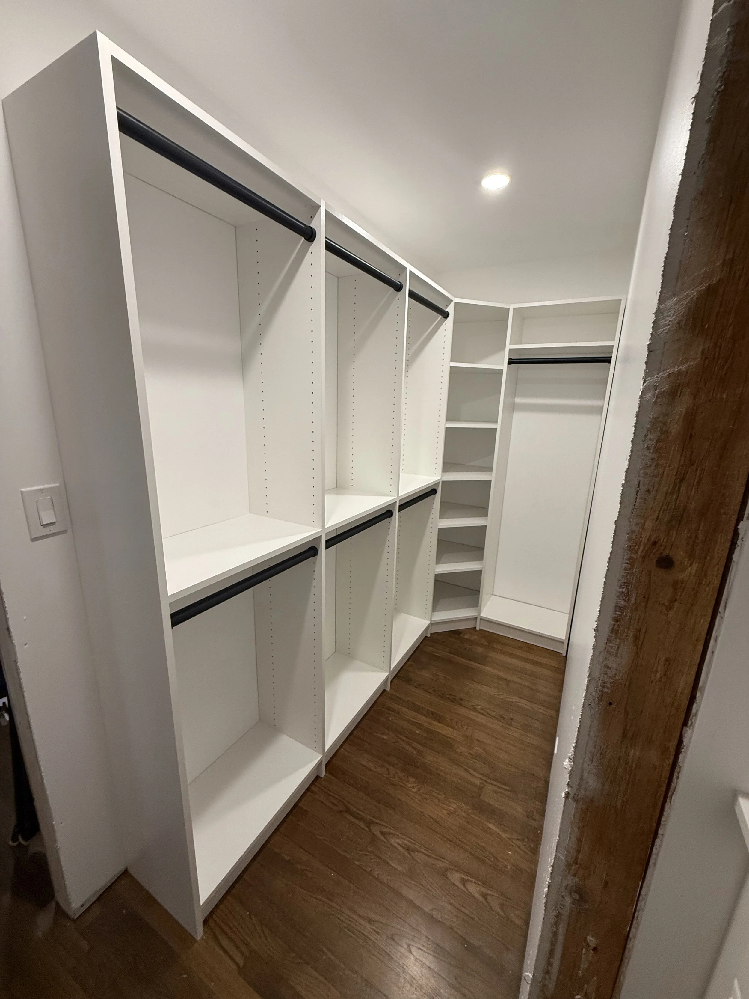 Empty custom closet with white shelving, black rods for hanging clothes, and wooden floor.