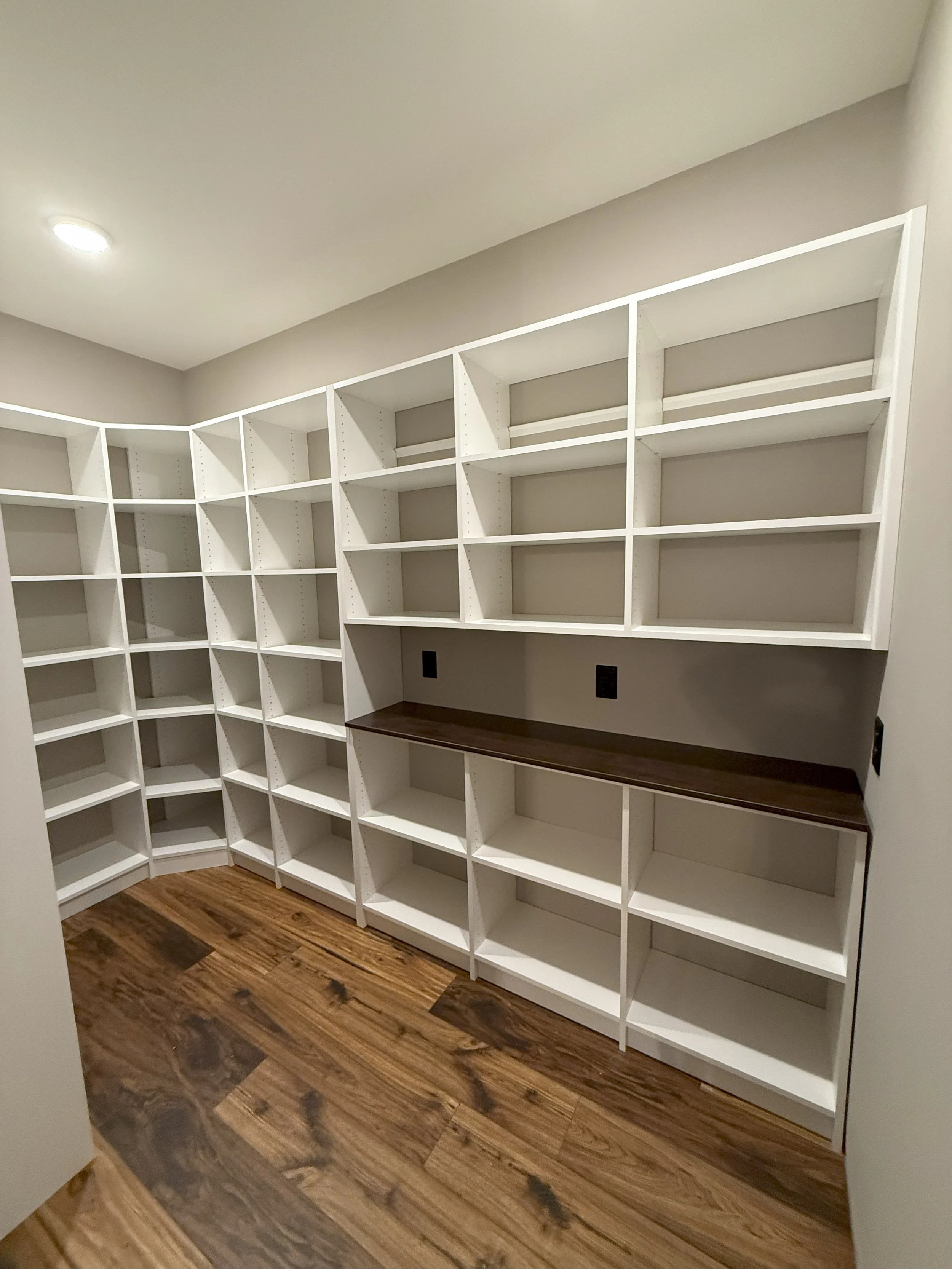 Empty white built-in shelves and cabinets in a corner of a room with hardwood flooring.