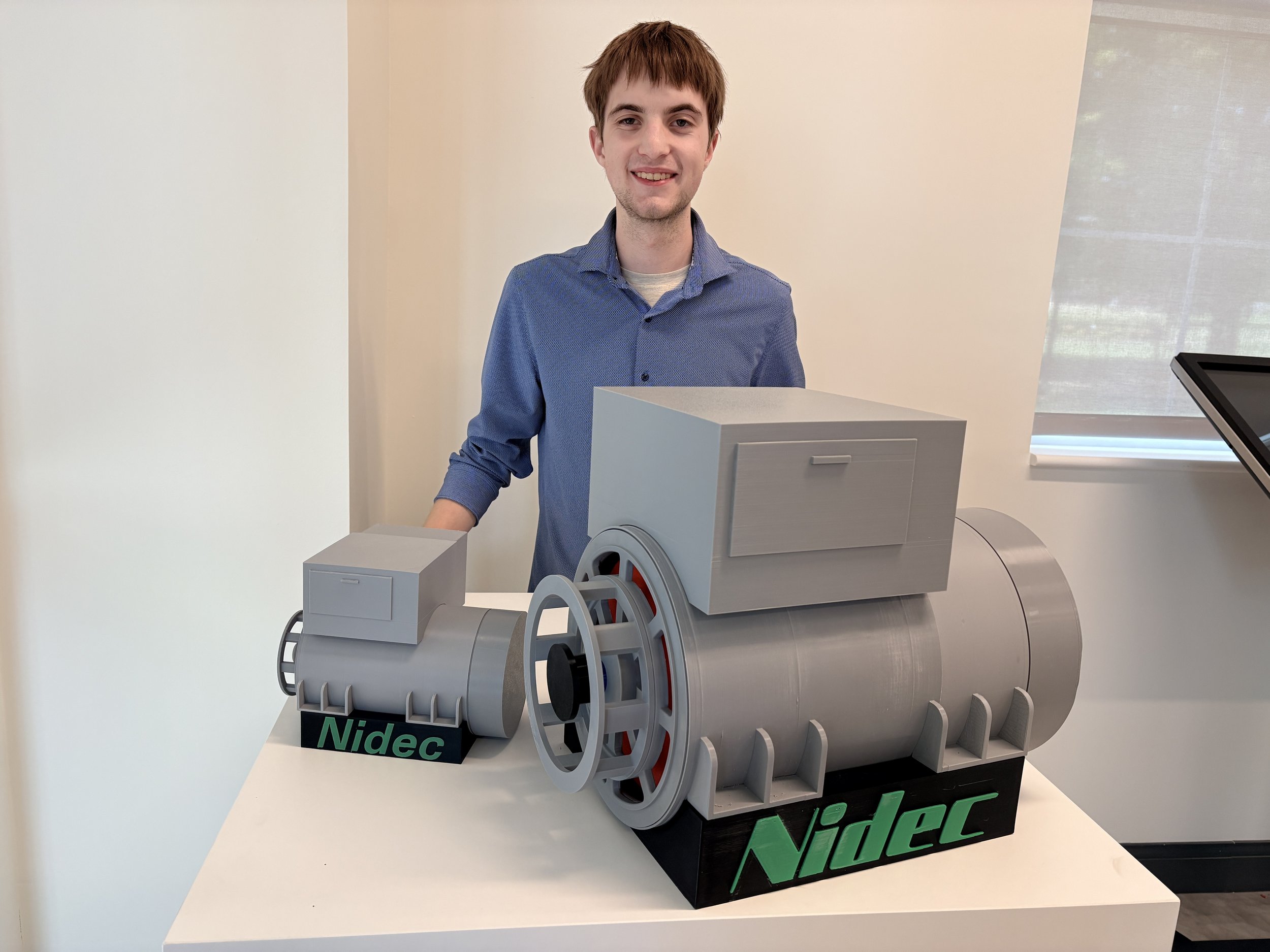 Student standing behind pedestal showcasing 2 3D printed alternators