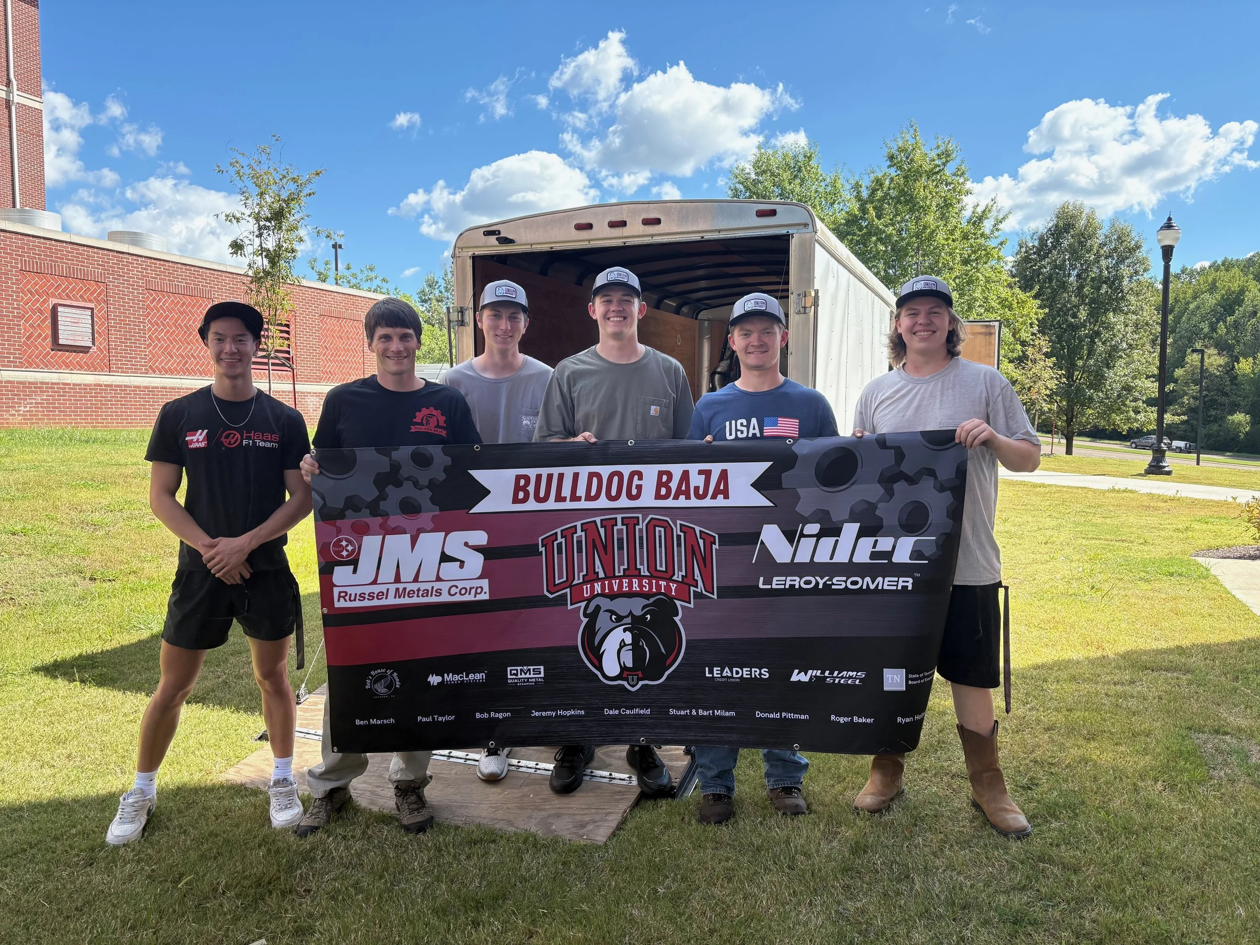 Four students and a professor holding the Bulldog Baja banner
