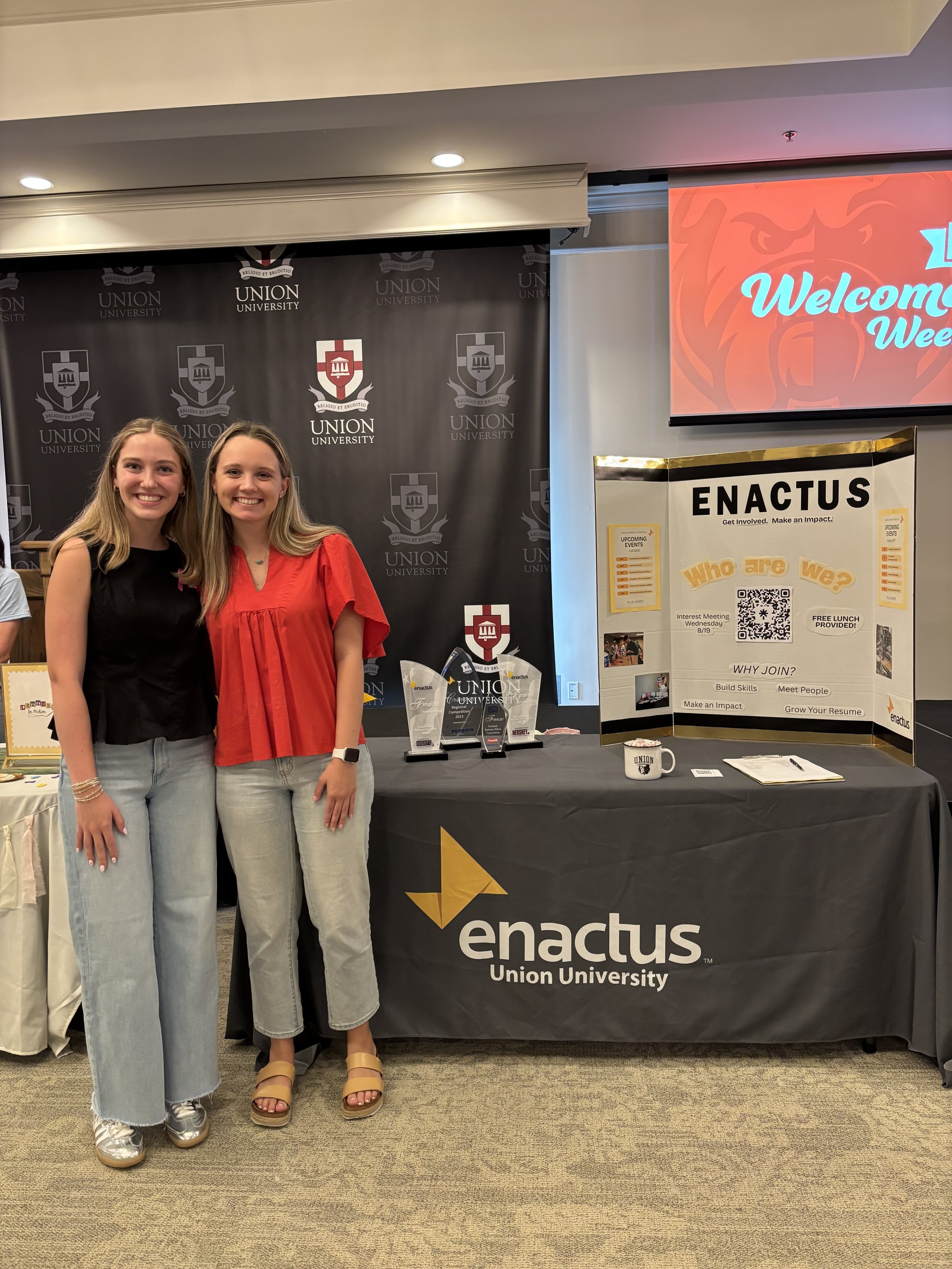 Two students standing by Enactus table