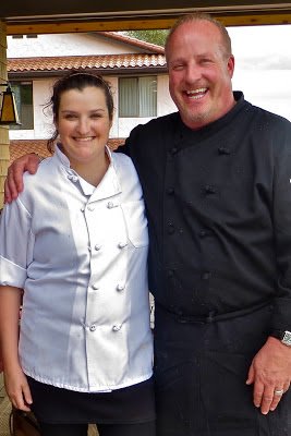 A woman and a man in chef uniforms smiling together outdoors.