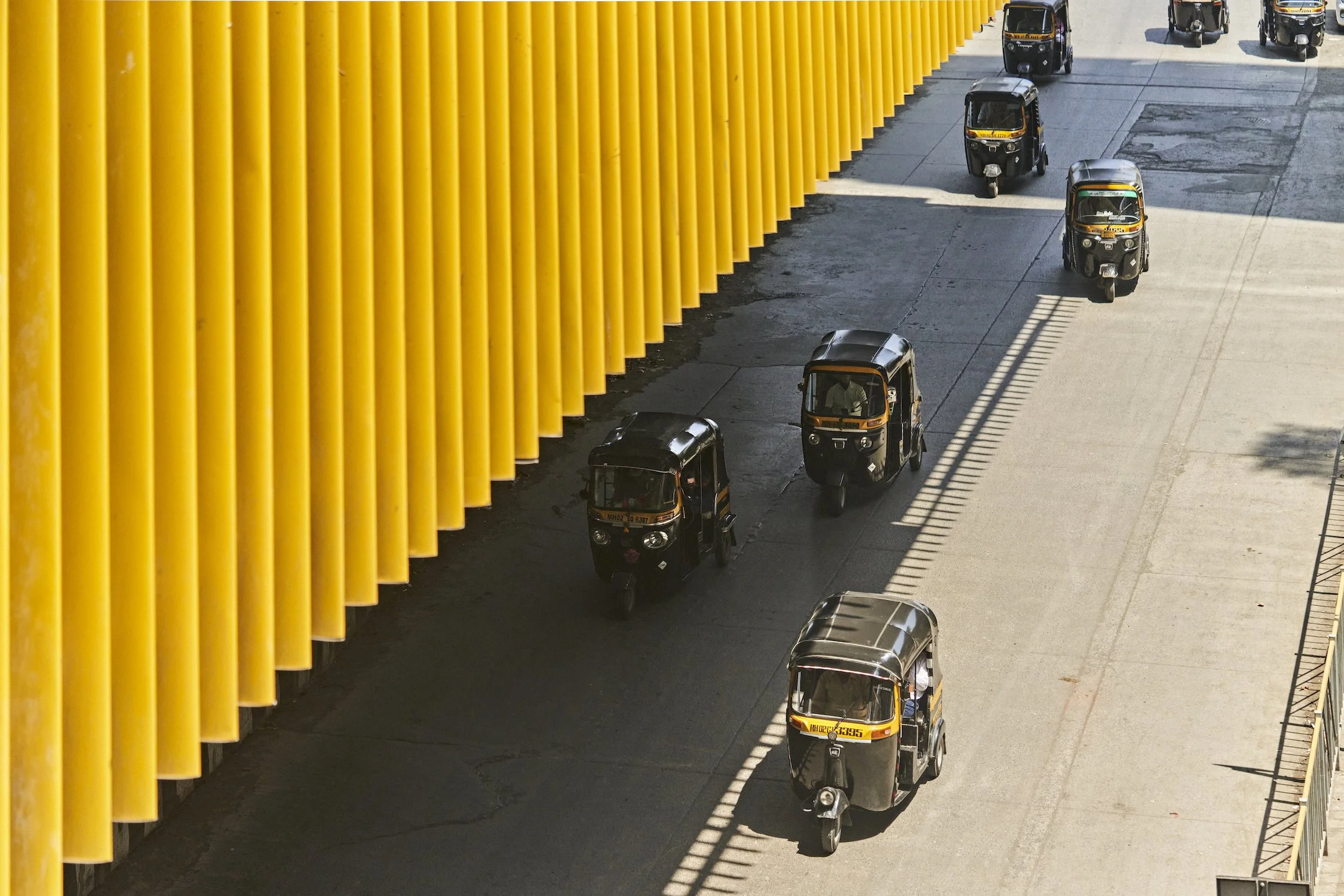 Auto rickshaws driving on a road next to a yellow wall