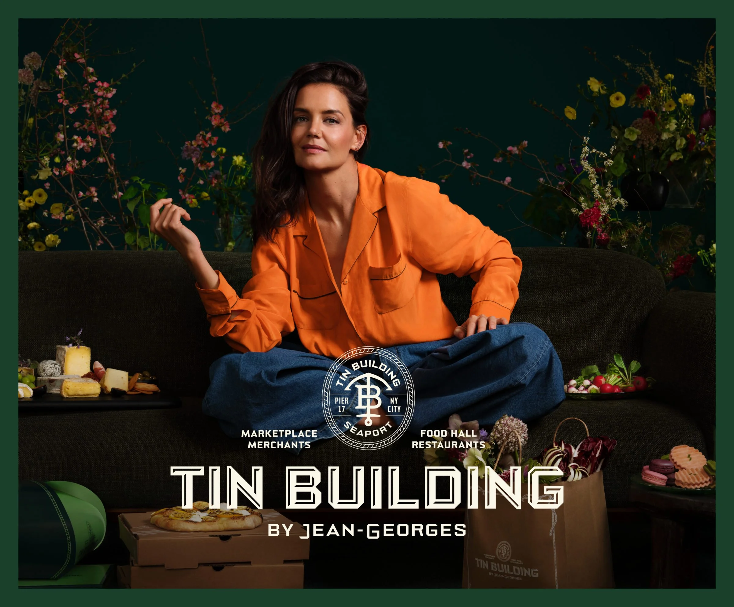 Woman sitting on a couch with flowers, Tin Building by Jean-Georges sign, food spread in the foreground.