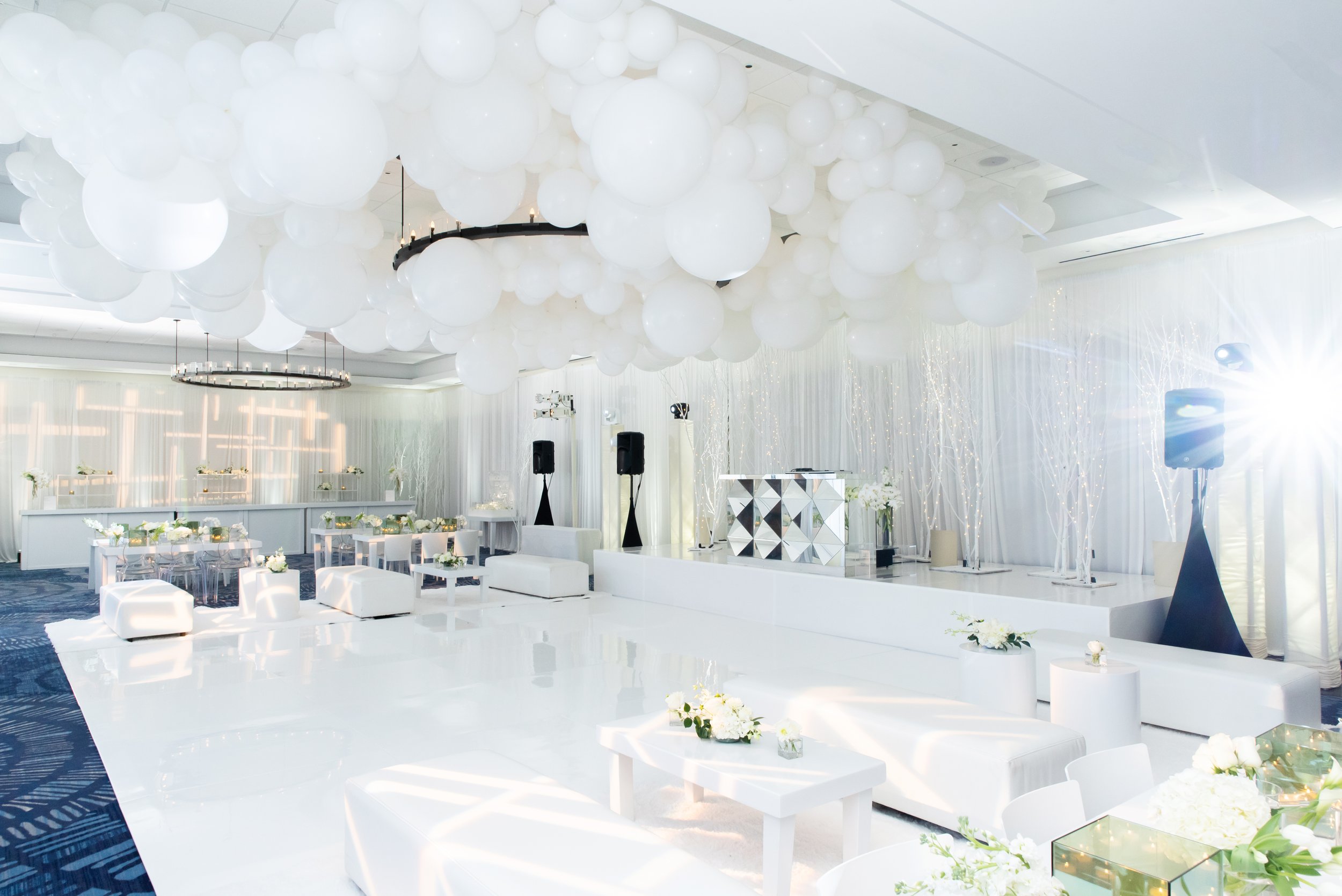  Elegant all-white luxury event in Newport Beach, featuring a modern dance floor, chic lounge seating, and a dramatic ceiling installation of white balloons, captured by Tiffany Perry Photography and Photo Booth Squared