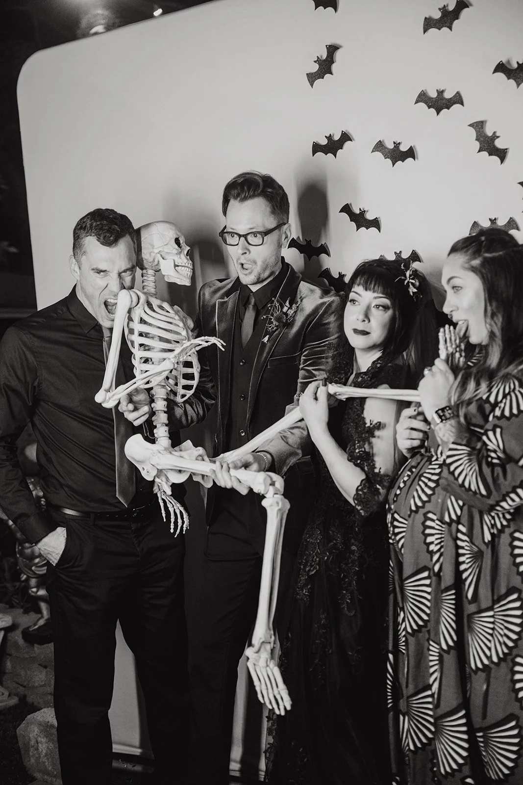 Spooky and fun Halloween-themed photo booth rental in Orange County, featuring guests posing with a skeleton prop against a bat-decorated backdrop. Perfect for Halloween parties, gothic weddings, and themed events. Captured by Tiffany Perry Photograp