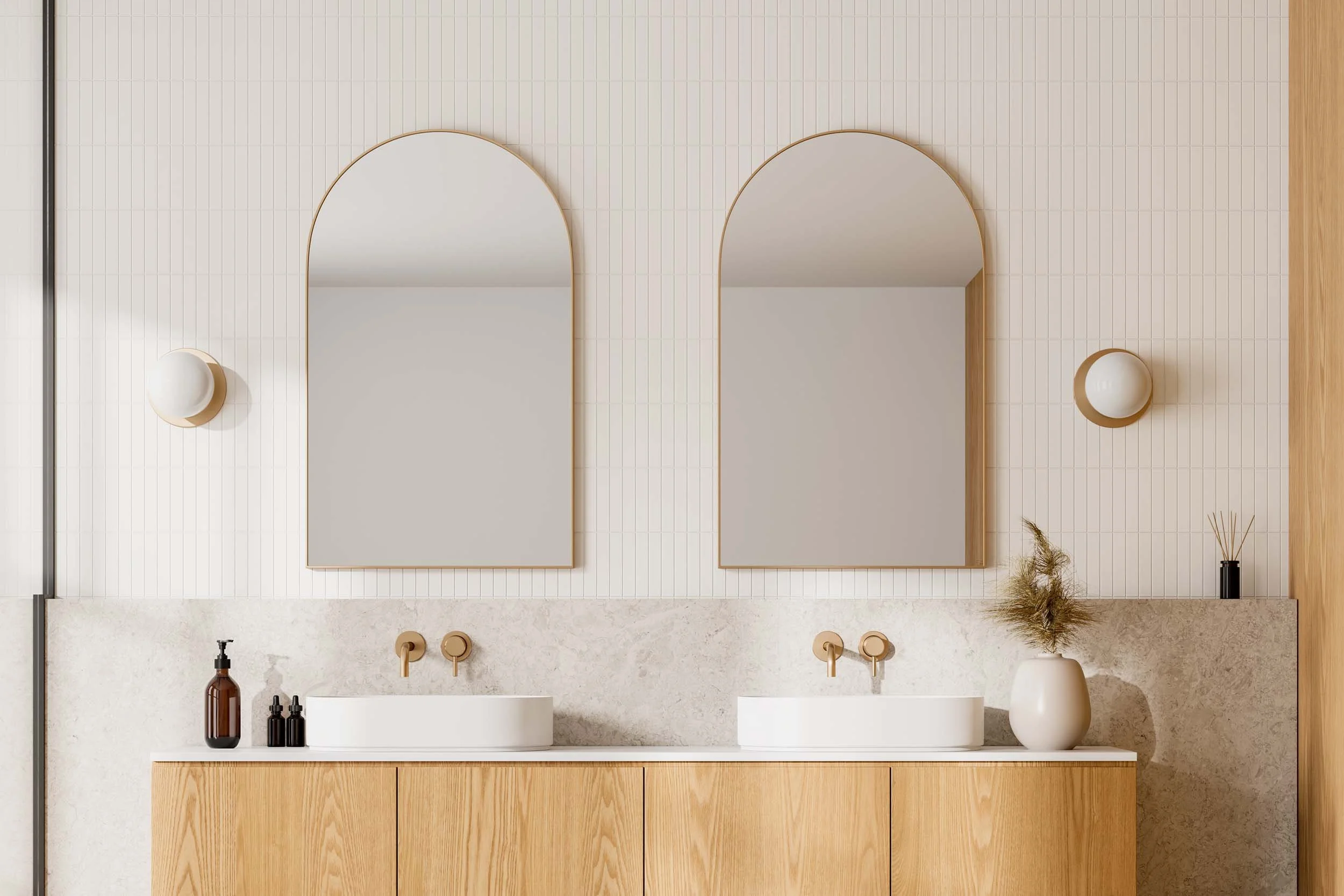 Bathroom vanity with two white vessel sinks, two large arched mirrors, and natural wood cabinet. Wall-mounted lights, decorative bottles, a vase with dried plants, and a reed diffuser.