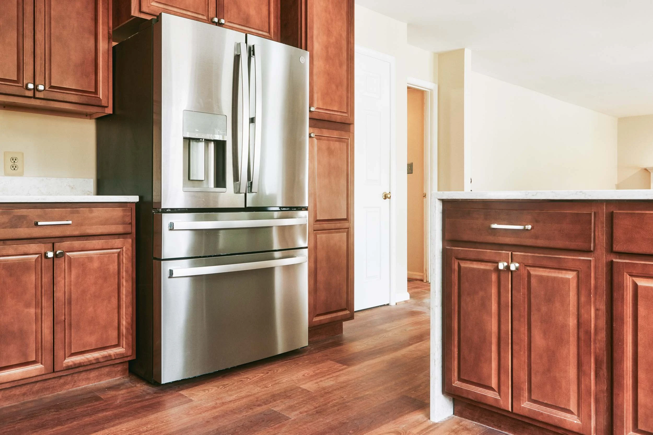 A kitchen with wooden cabinets, a stainless steel refrigerator, and a wooden floor.