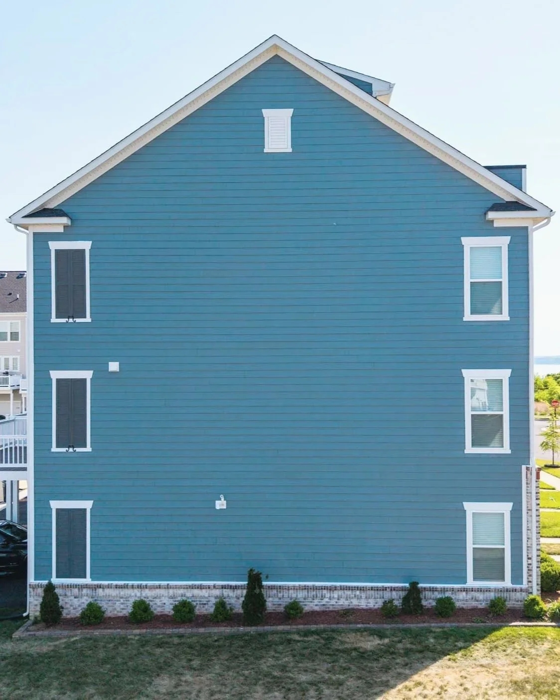 A blue, three-story residential building with six windows and white trim, with small bushes and a lawn in front.