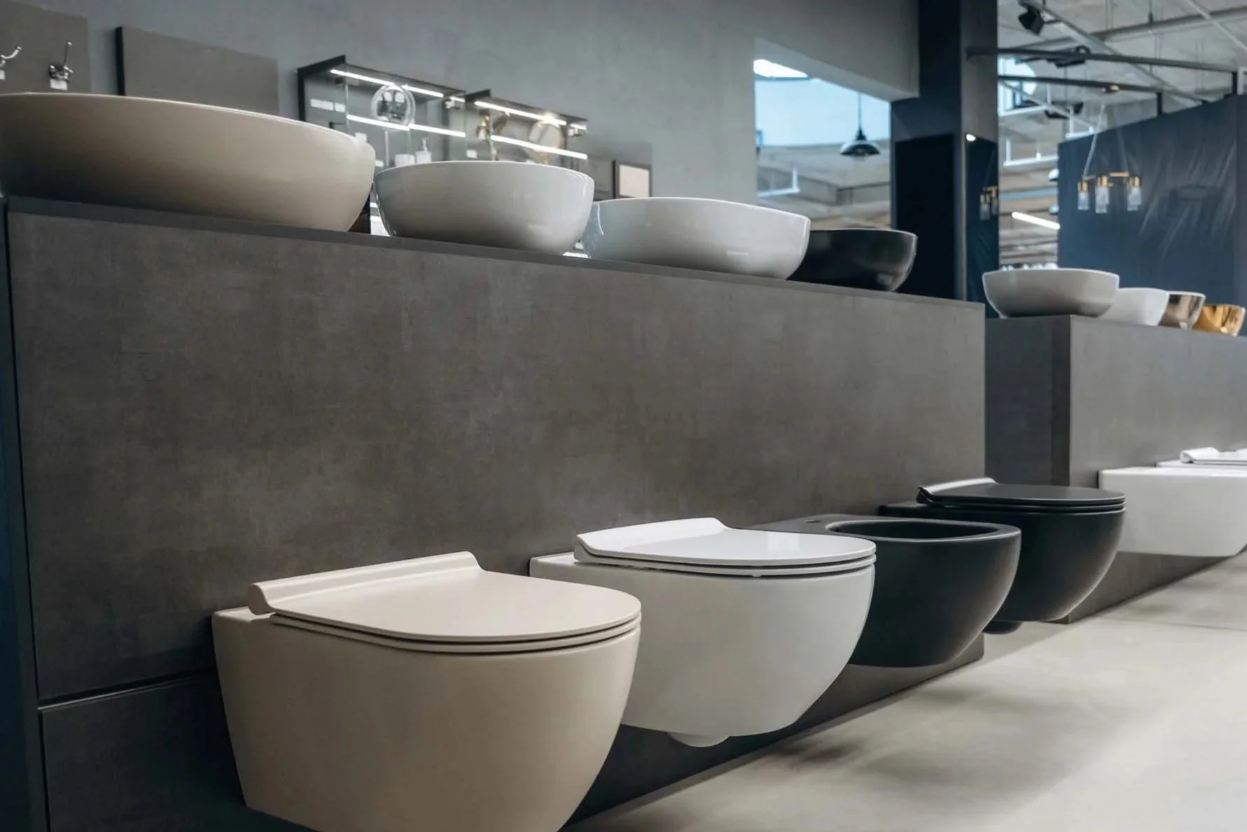 Bathroom fixtures on display, including white and black toilets and bowls, in a showroom with modern industrial design.