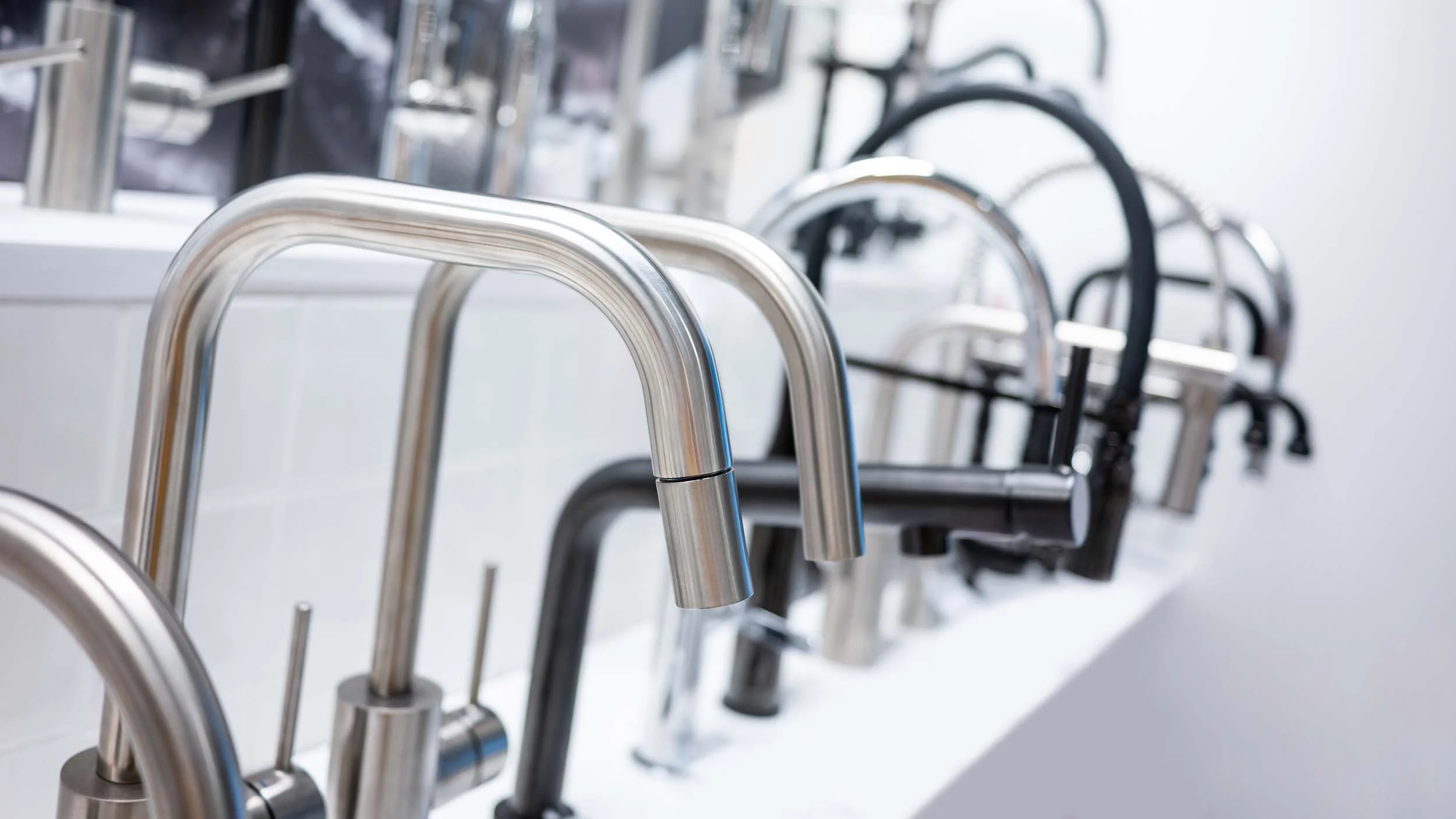 Multiple modern kitchen faucets in silver and black in a row