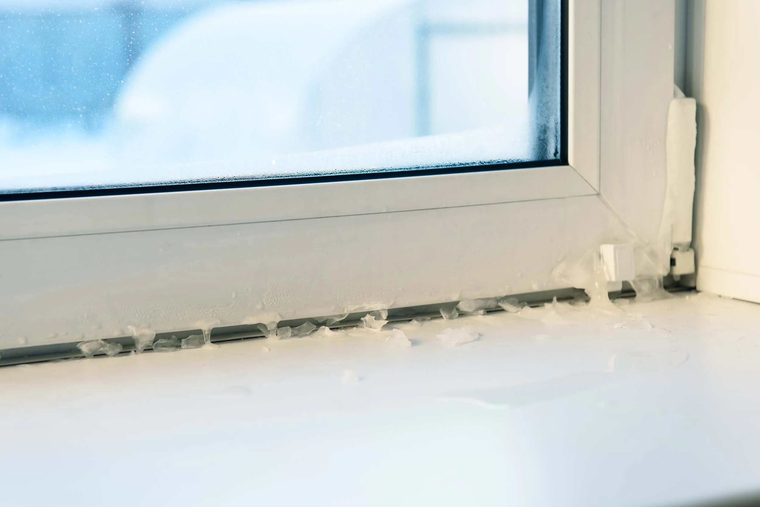 Close-up of a window frame with icicles formed at the bottom edge.