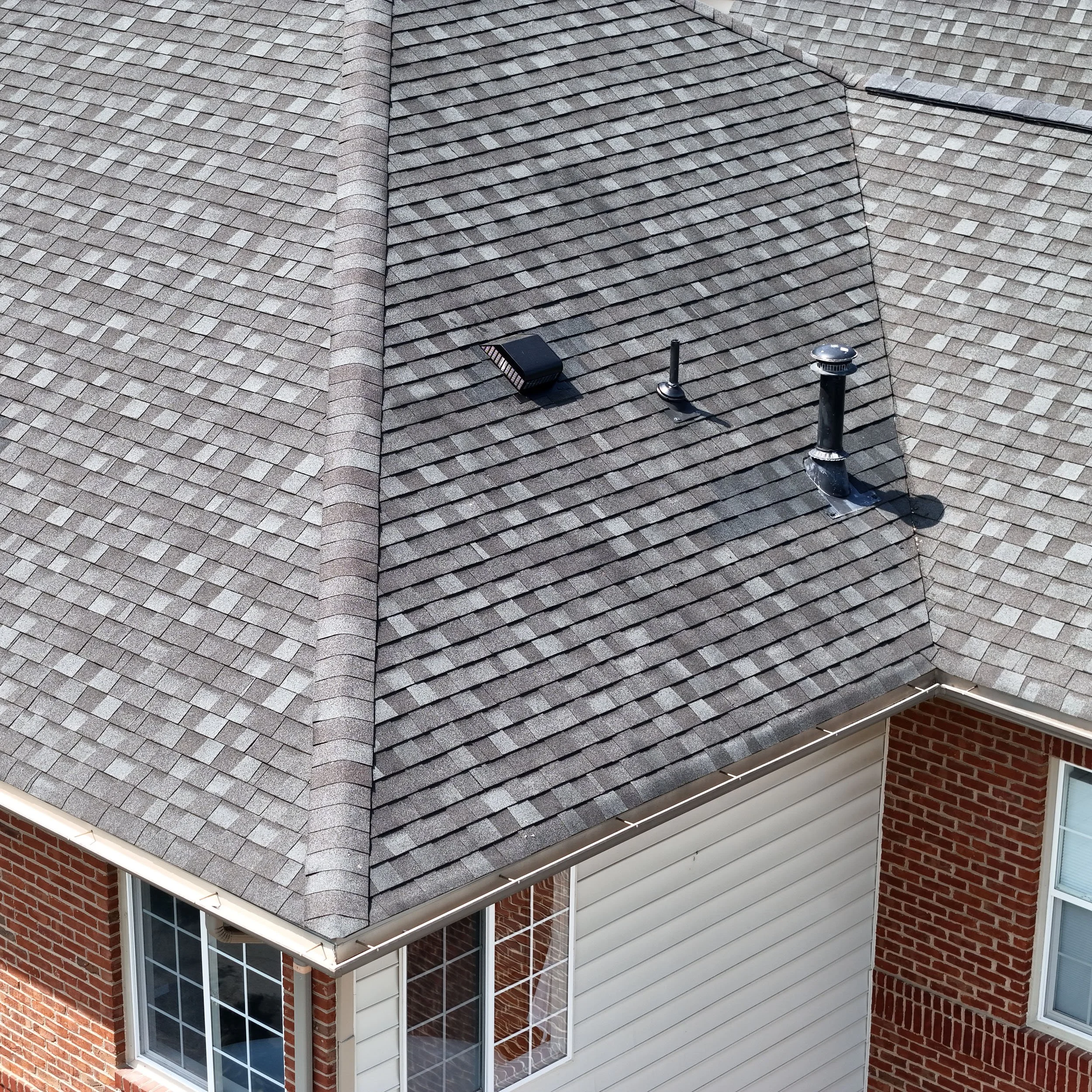 Aerial view of a house roof with multiple sections covered in gray asphalt shingles, including vents and a small solar panel.