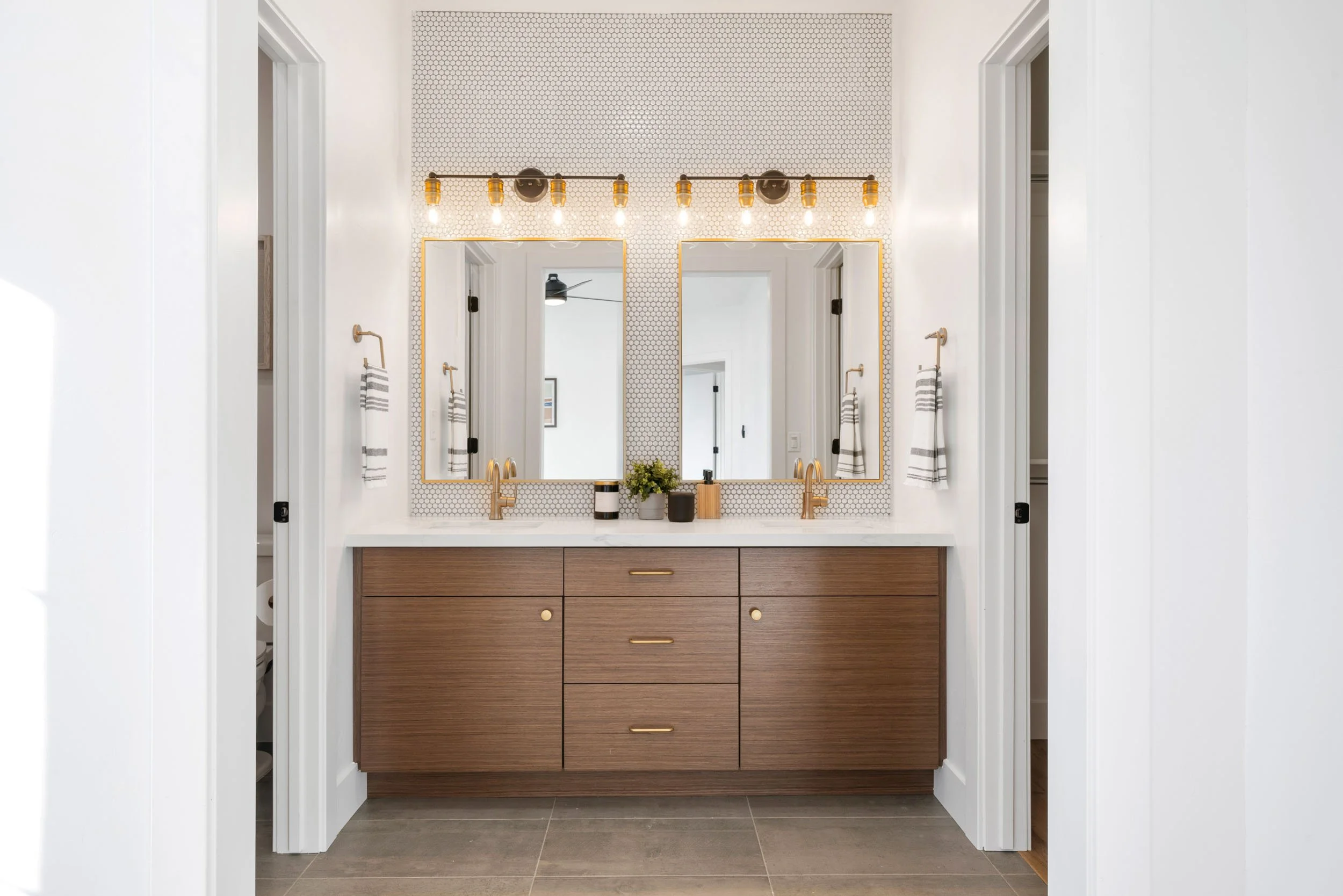 Modern bathroom vanity with dual mirrors, gold fixtures, and a wood cabinet, illuminated by overhead lighting.