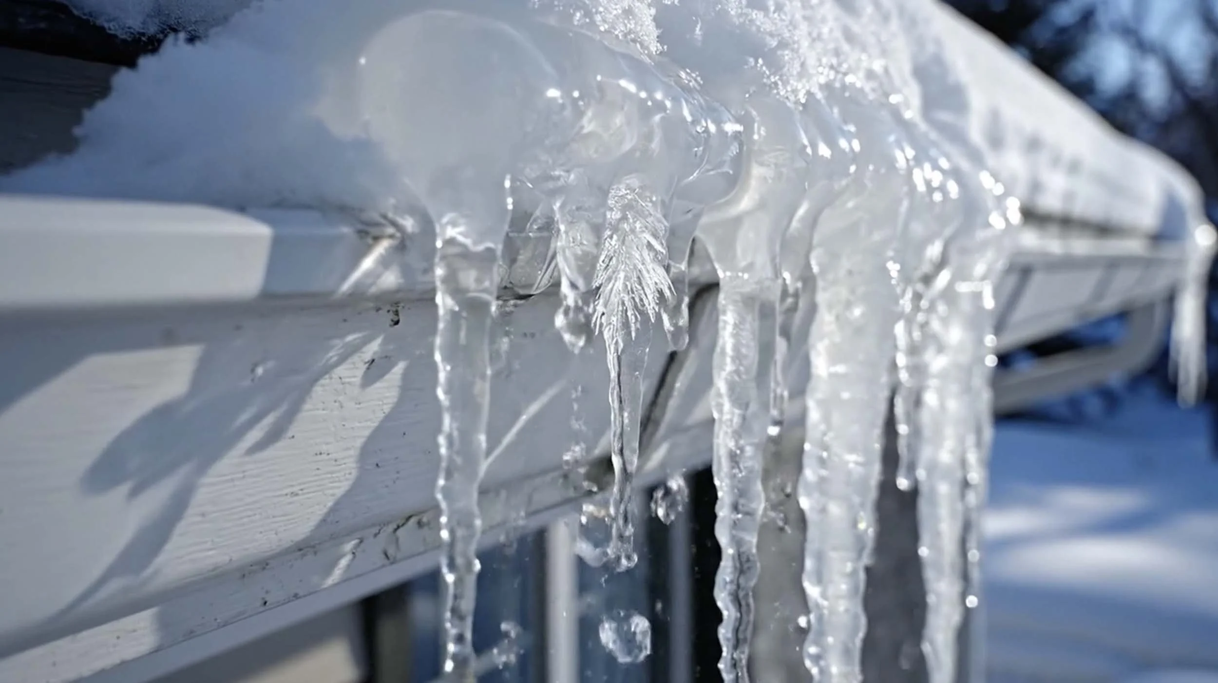 Icicles hanging from a white metal surface outdoors in winter.