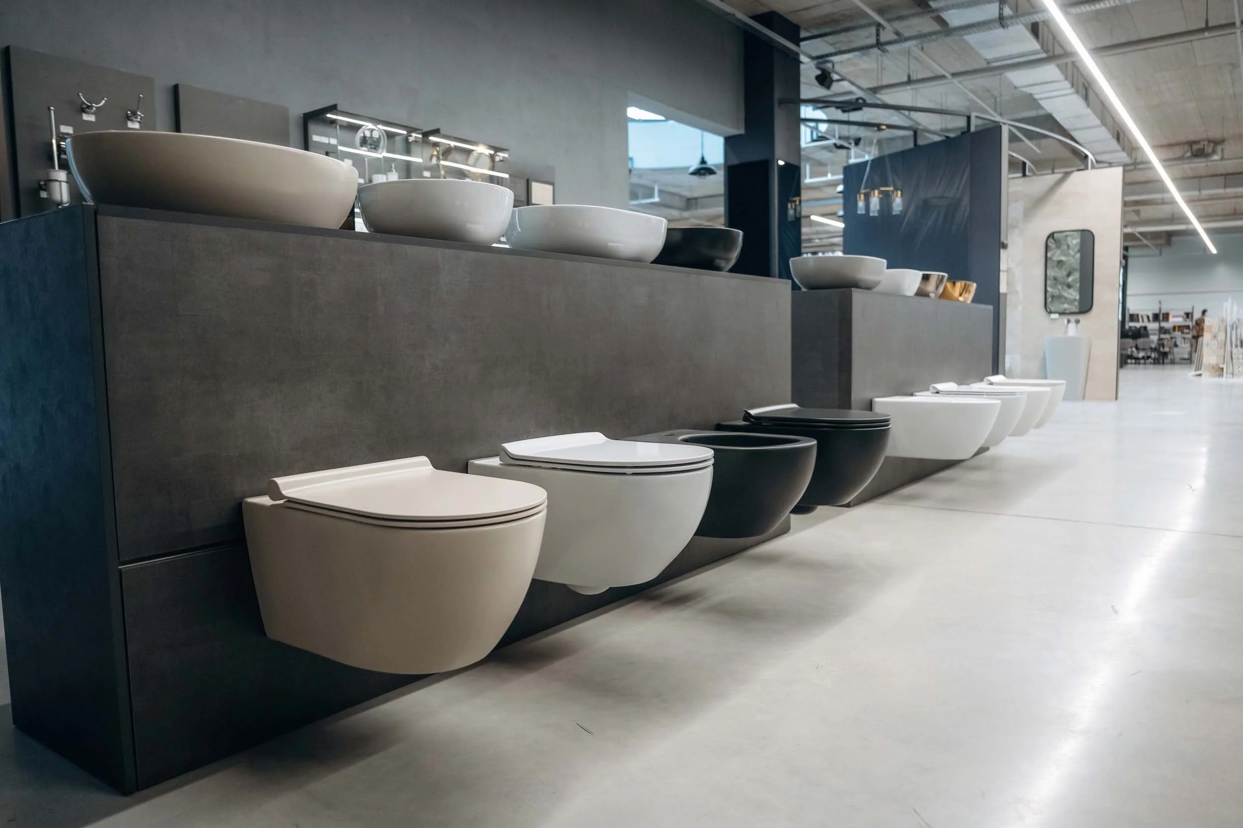 Bathroom fixtures display in a store with various modern toilets and bowls arranged on a black display stand in a spacious retail environment.