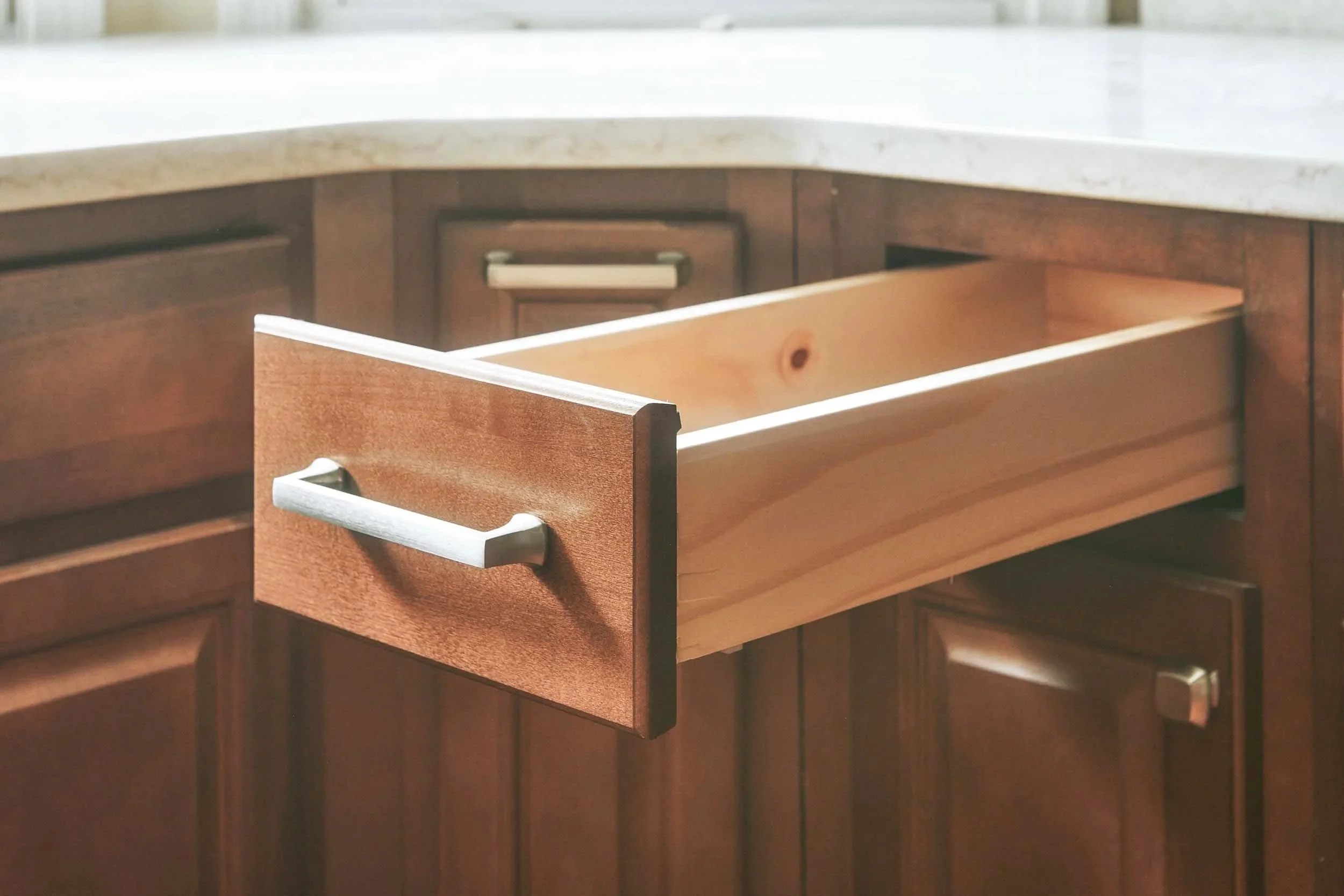 Open kitchen drawer in wooden cabinet with a marble countertop.