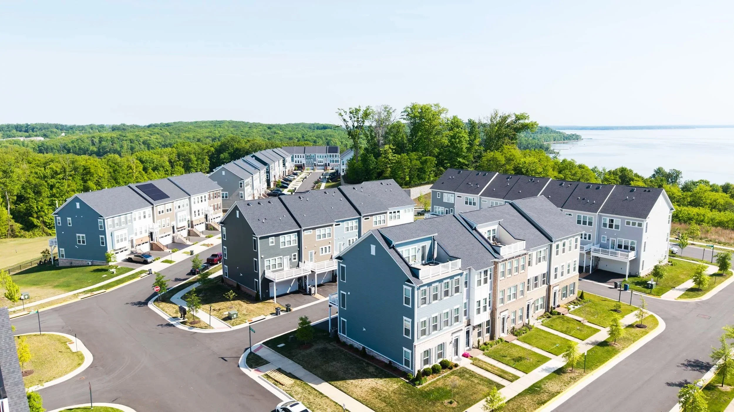 Aerial view of modern residential apartment complex near a river, surrounded by green trees and landscaping.