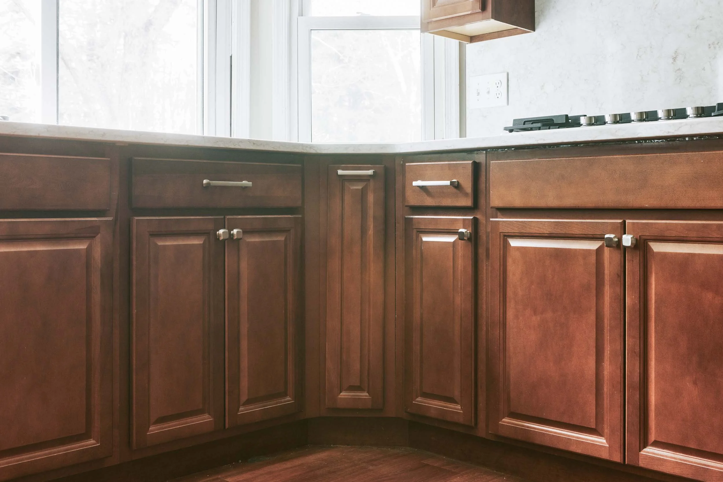 Kitchen with brown wooden cabinets, marble countertop, and a gas stove. Window above the counter allowing natural light.