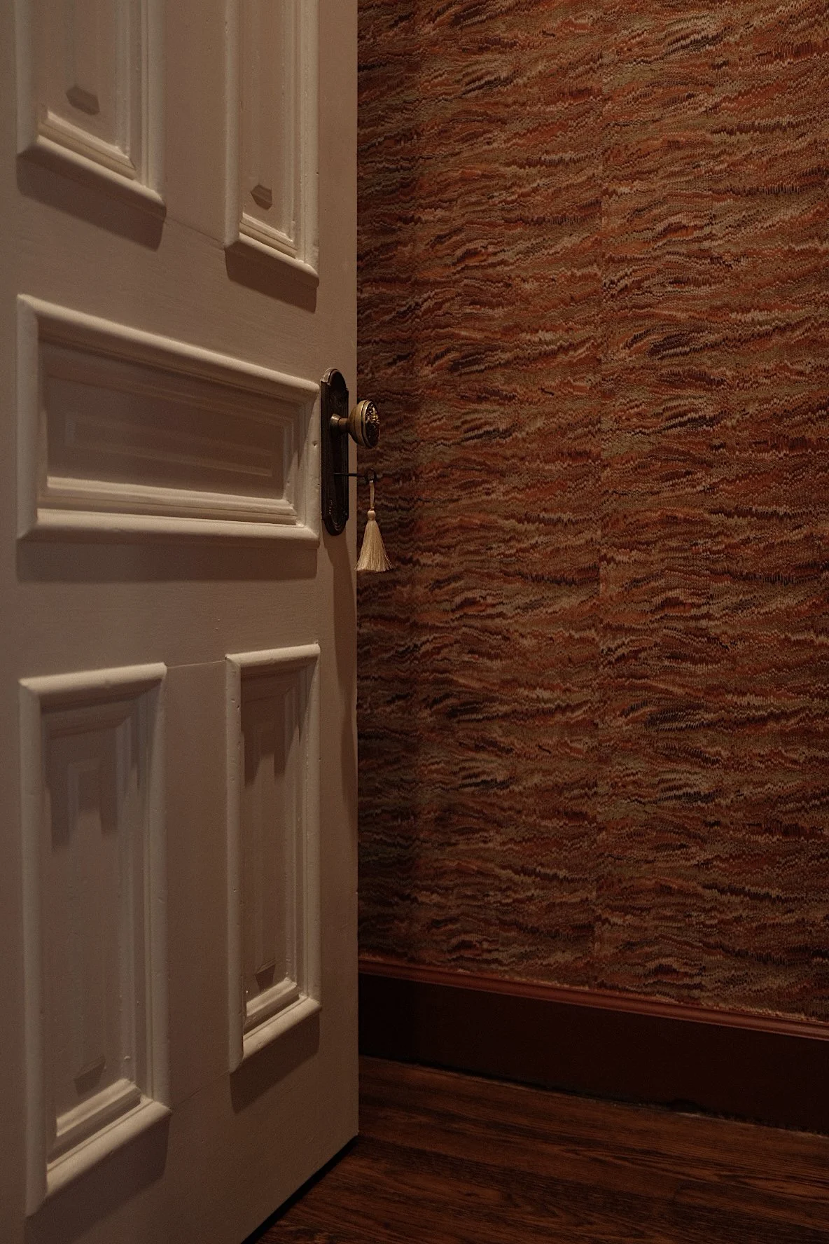 A white door partially open revealing a textured brown and red wavy wallpaper on the wall behind it.
