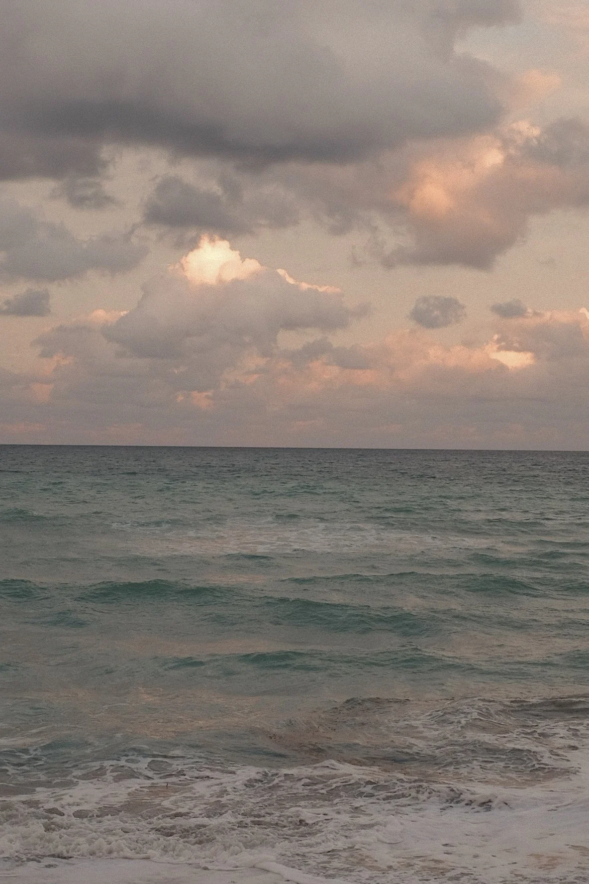 Ocean waves with a cloudy sky and some pink-tinged clouds at sunset.