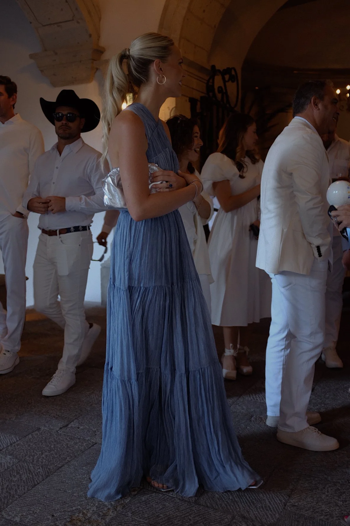 Group of people dressed in formal attire, including a woman in a blue gown and a man in a cowboy hat, in a dimly lit venue.