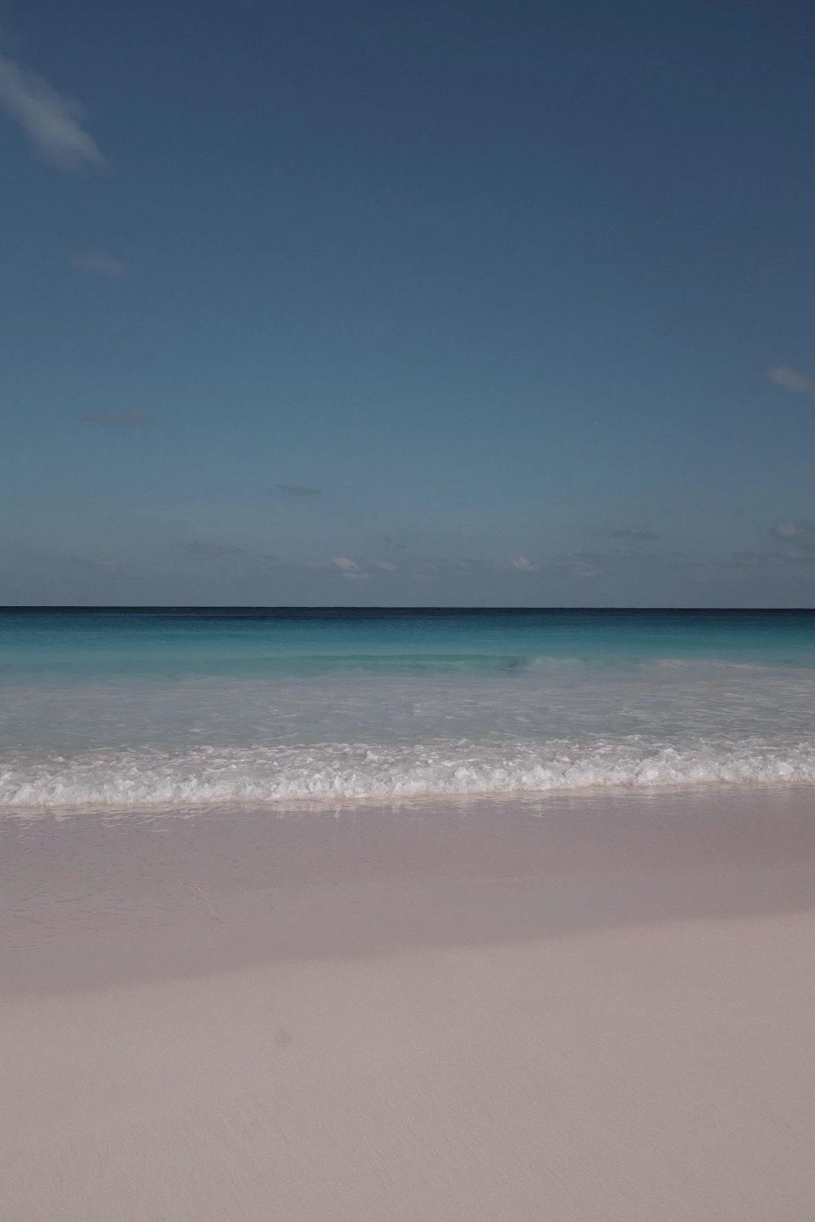 Sandy beach with gentle ocean waves and clear blue sky.