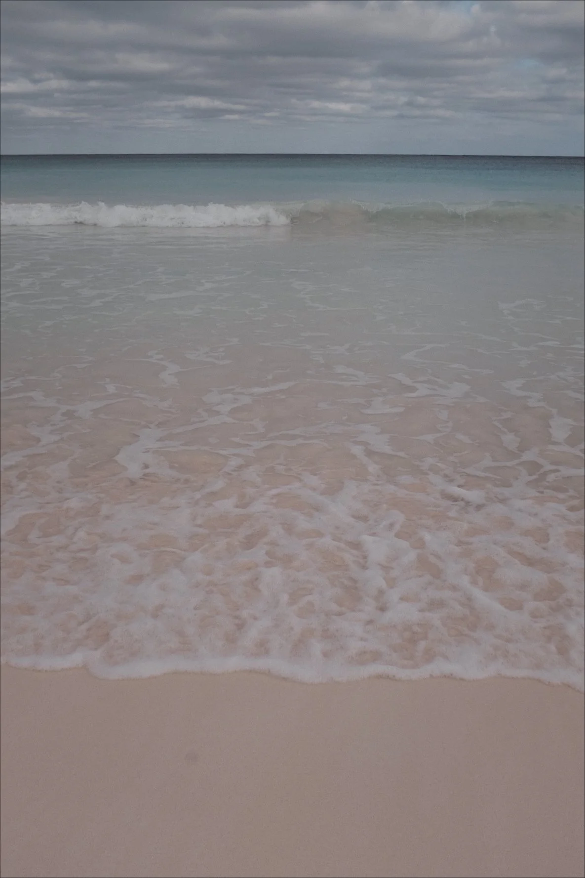 Pink sand beach with gentle ocean waves and a cloudy sky