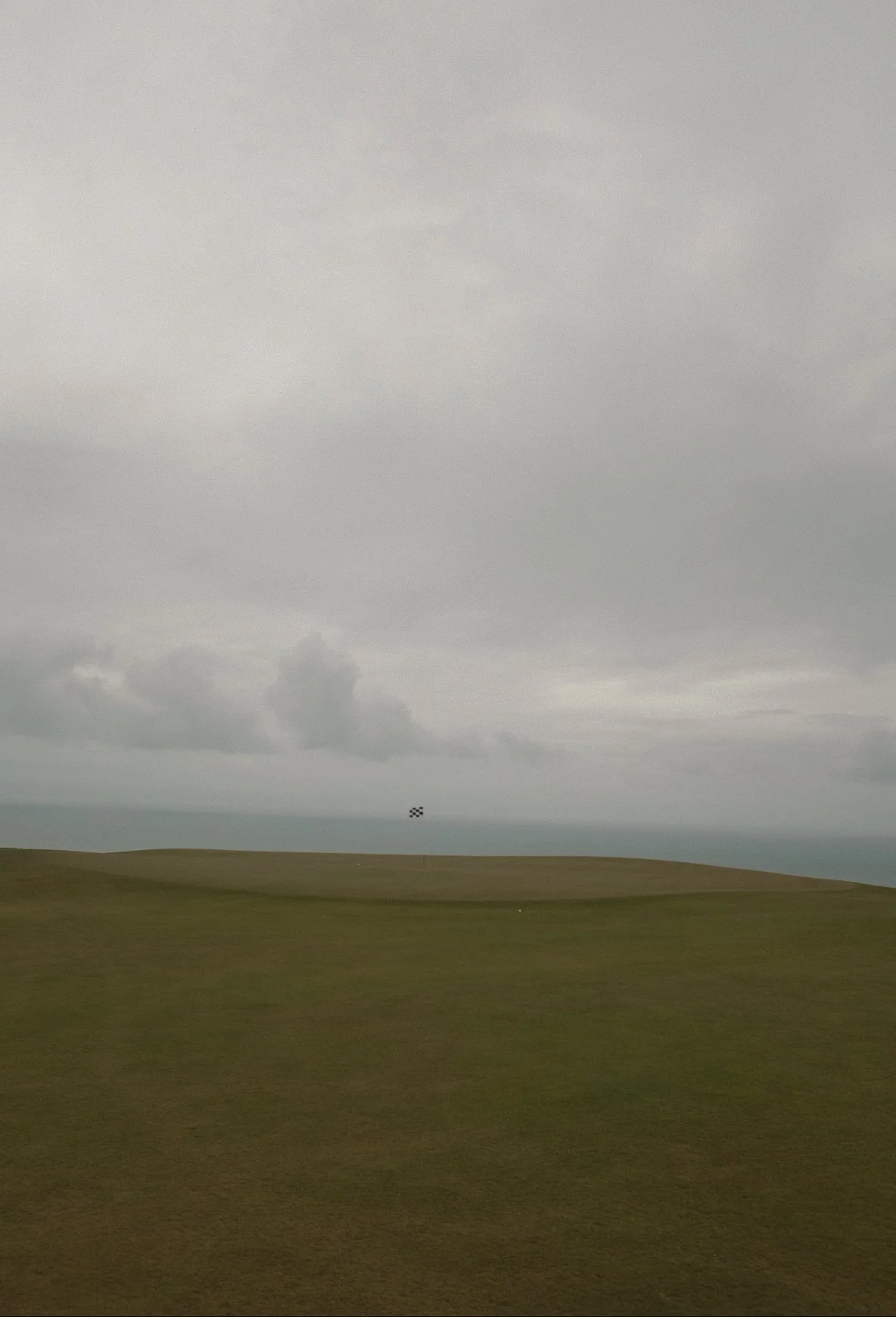 Golf course with a checkered flag, cloudy sky, and ocean in the background.