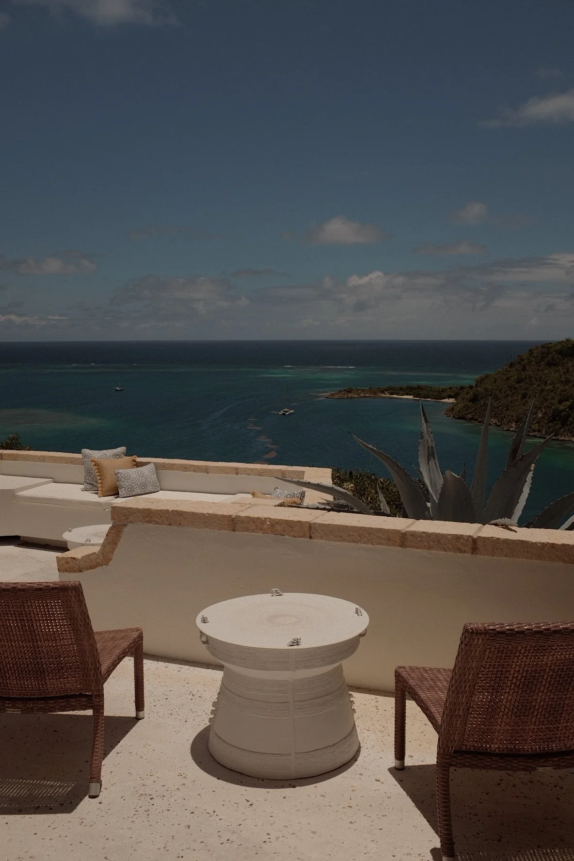 Outdoor patio with wicker chairs, small round table, and a view of the ocean and islands.