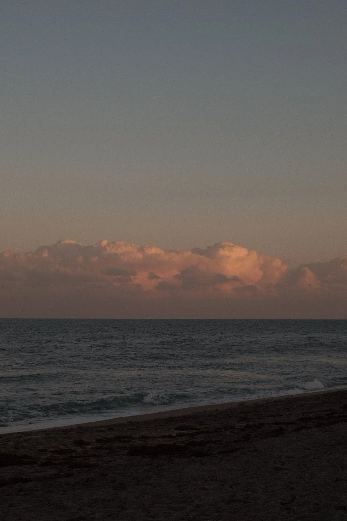 Sunset over the ocean with pink and orange clouds in the sky and gentle waves on the shore.