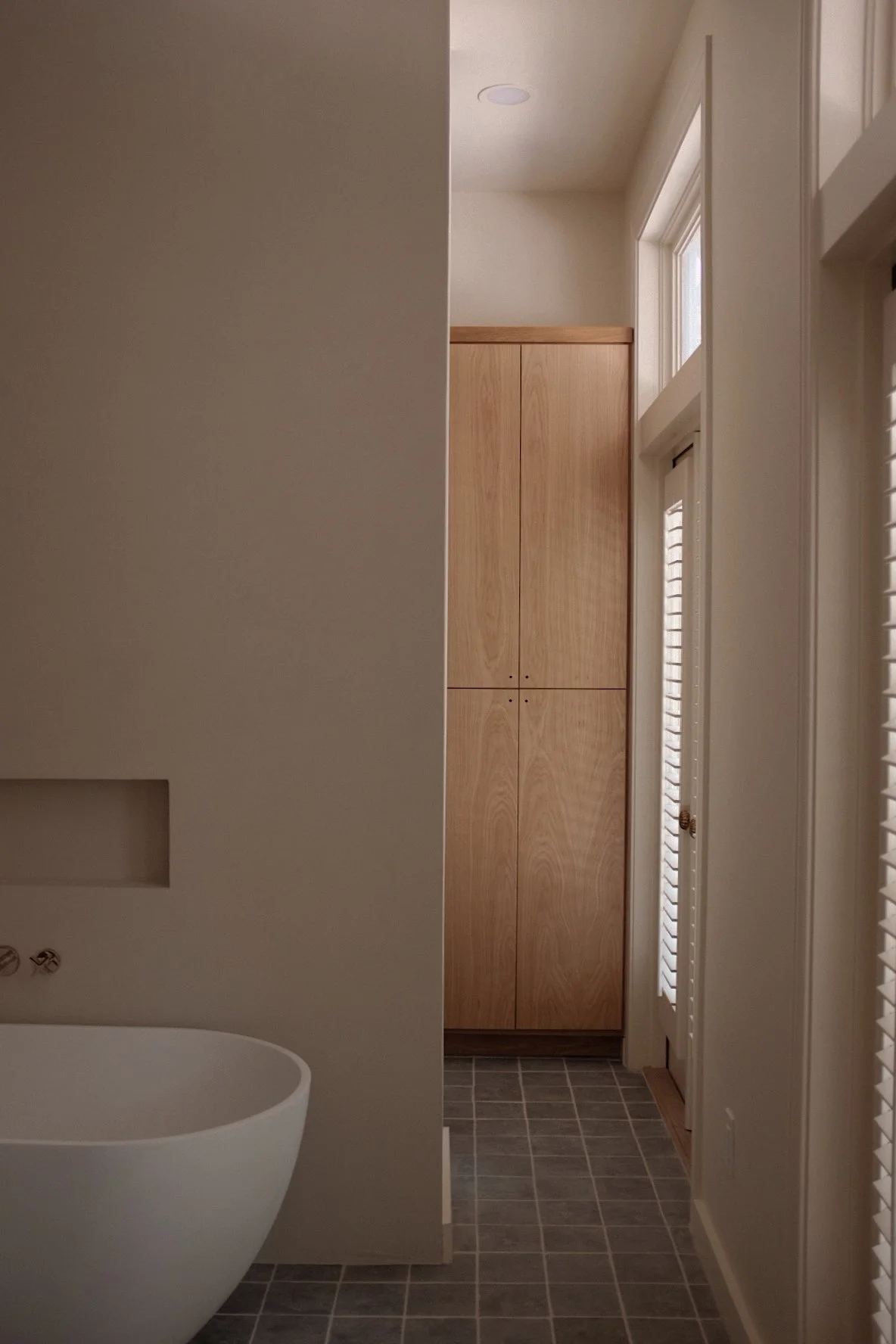 View of a bathroom with wooden cabinets, a white toilet, and a tiled floor, partially visible from the doorway.