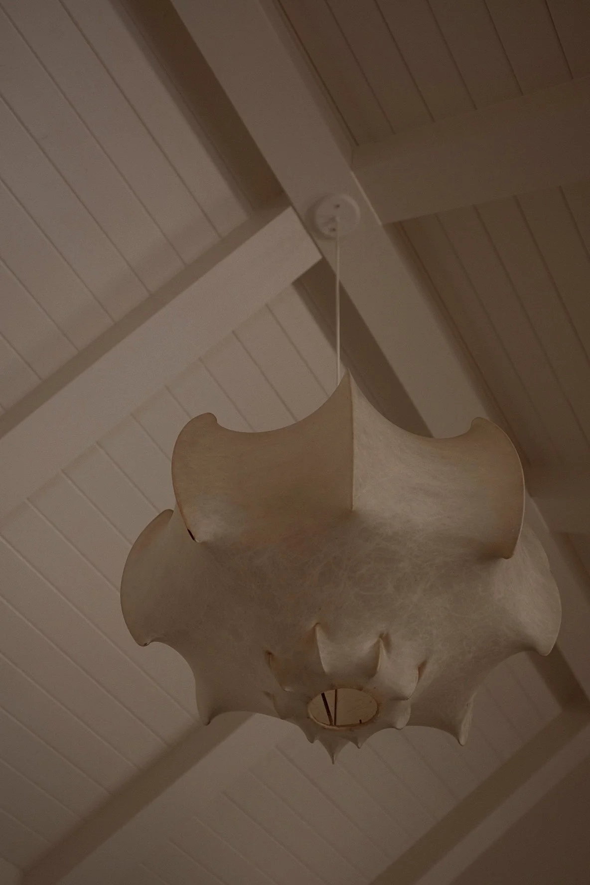 Hanging beige lampshade with scalloped edges from a white ceiling with wooden paneling.