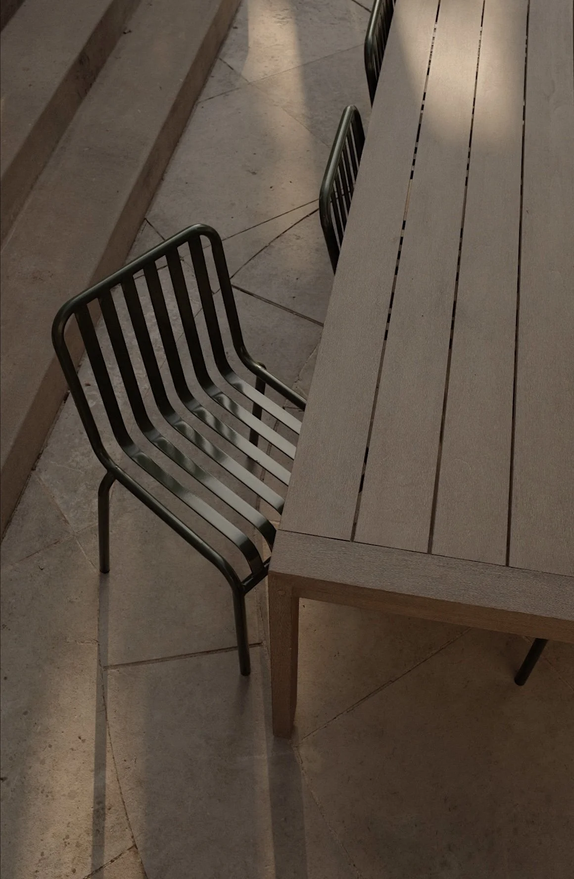 A black metal chair with horizontal bars to sit on, positioned next to a light-colored wooden table with a slatted top surface.
