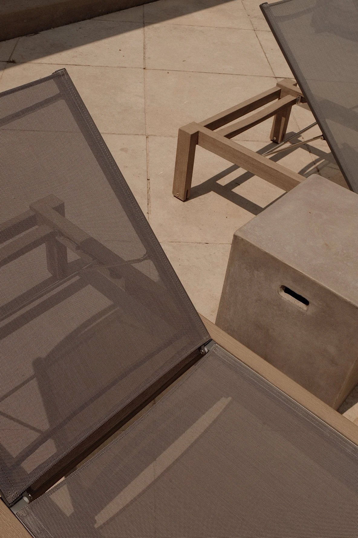 Outdoor patio with beige lounge chairs and a small concrete side table on a tiled floor.